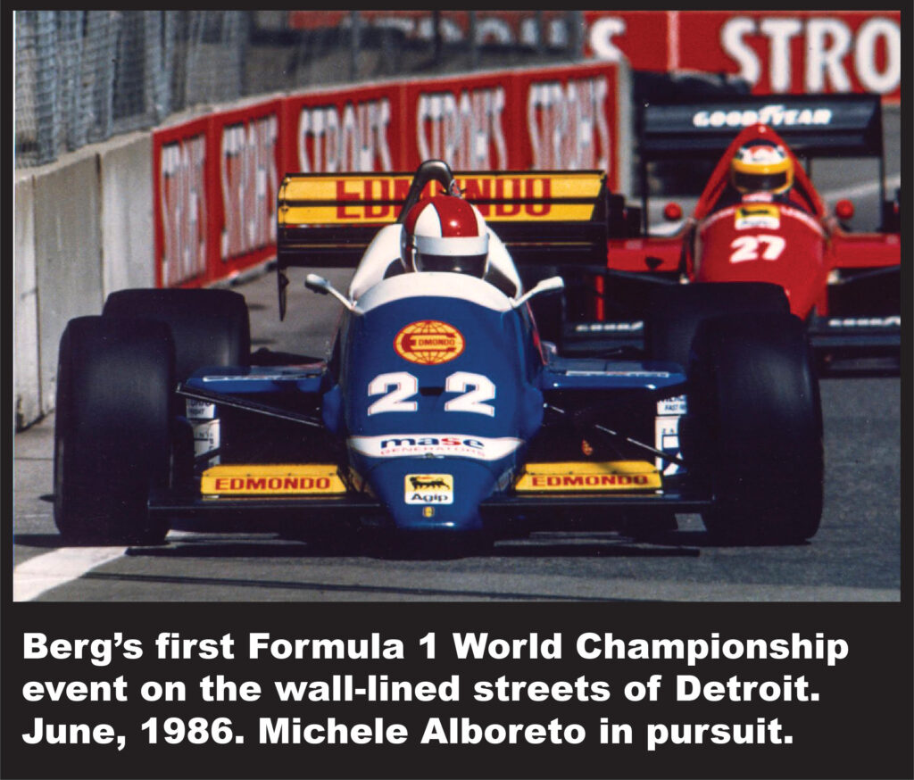 Blue formula 1 race car number 22 with edmondo sponsorship leading a red car number 27 on a street circuit with concrete barriers and goodyear signage