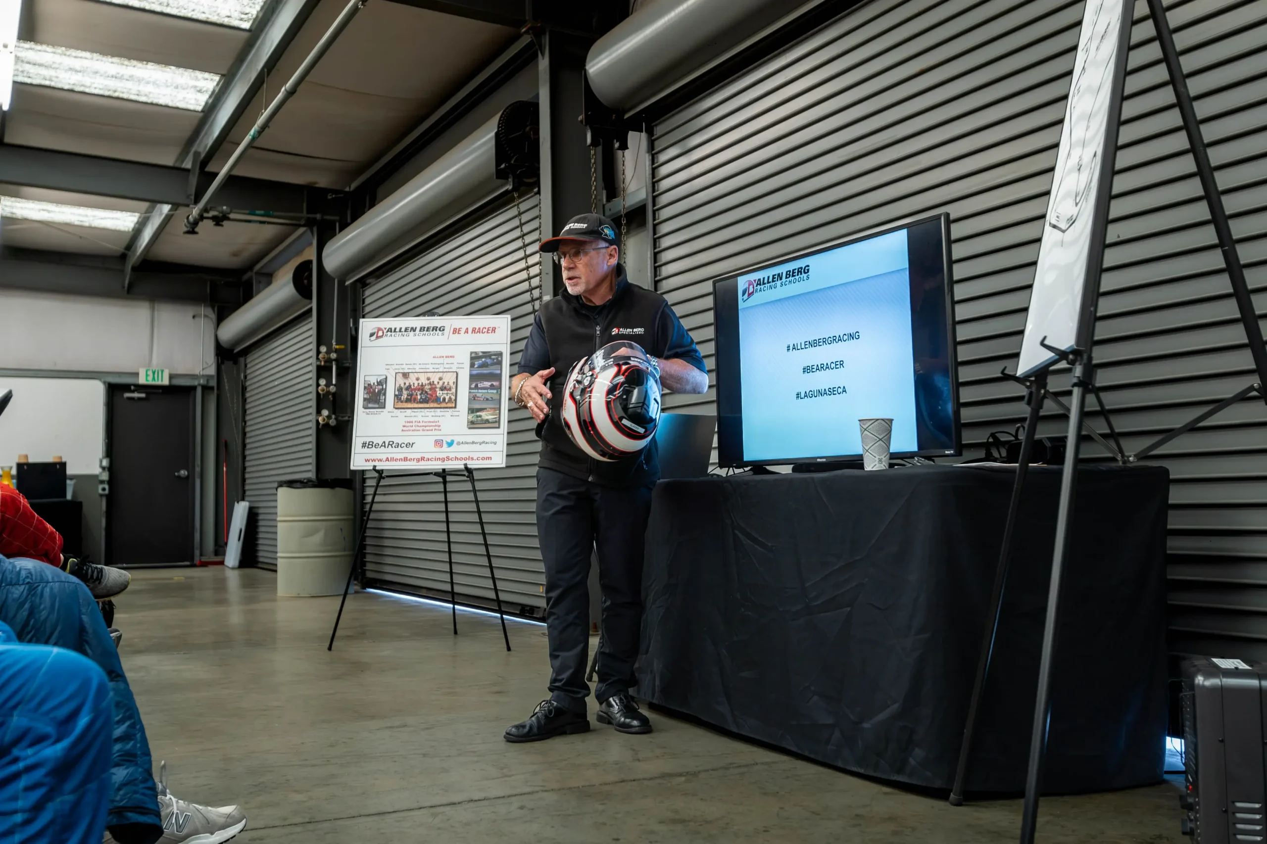 Instructor presenting helmet safety techniques in front of a presentation screen in the garage