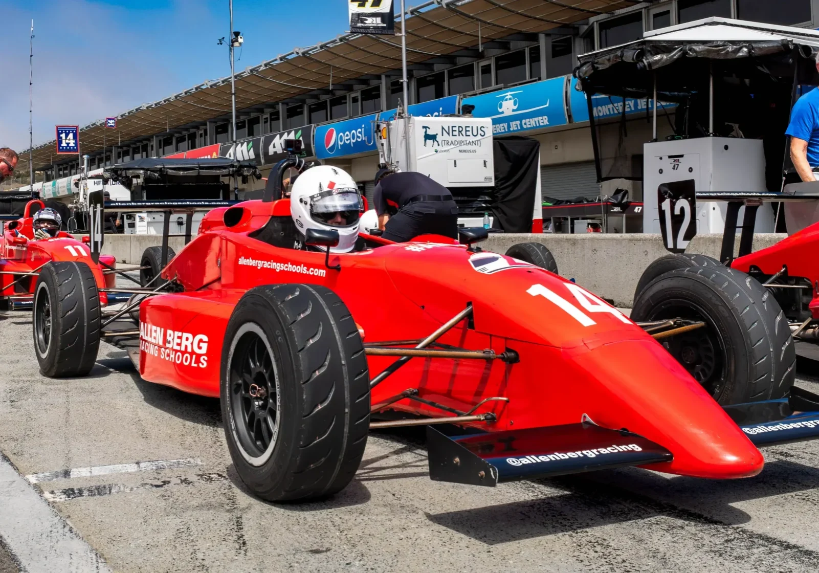 Red formula race car number 14 sitting staged in pit lane with a driver wearing a helmet