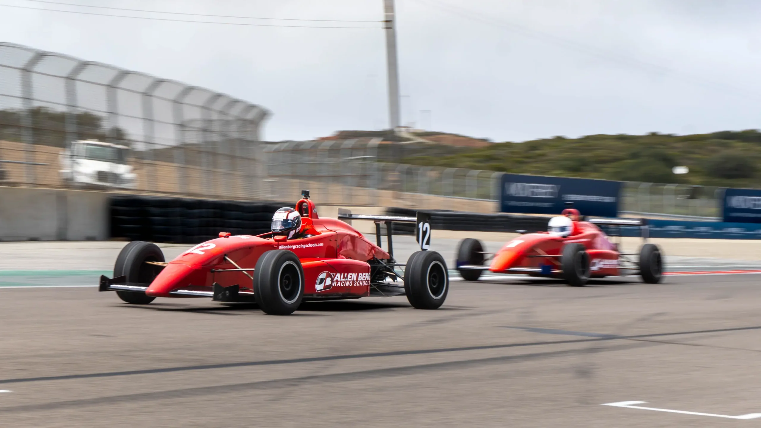 Red formula race car number 12 leading car number 3 along the race track during a session