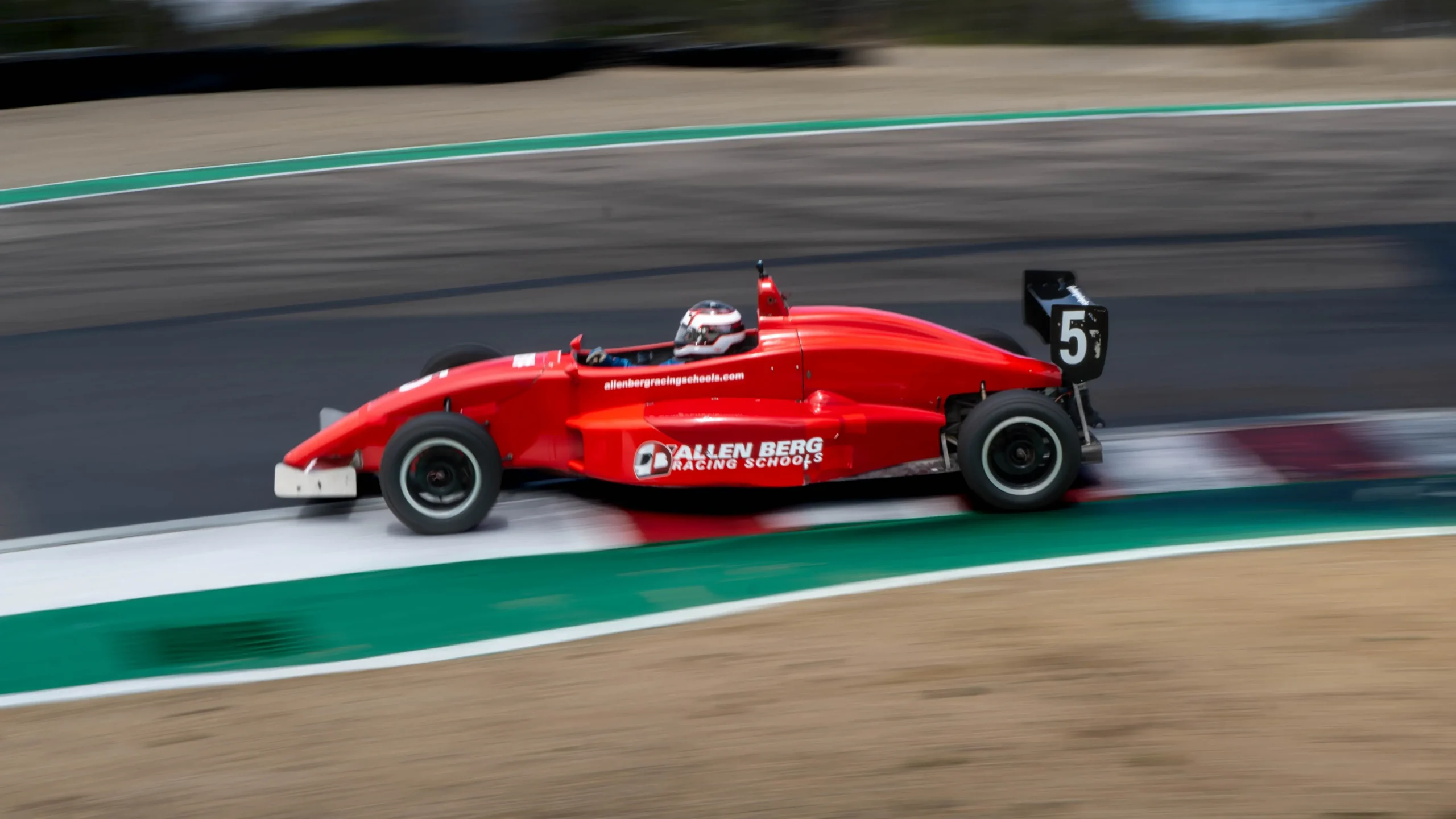 Side profile of red formula race car number 5 speeding along the track curbing at allen berg racing schools