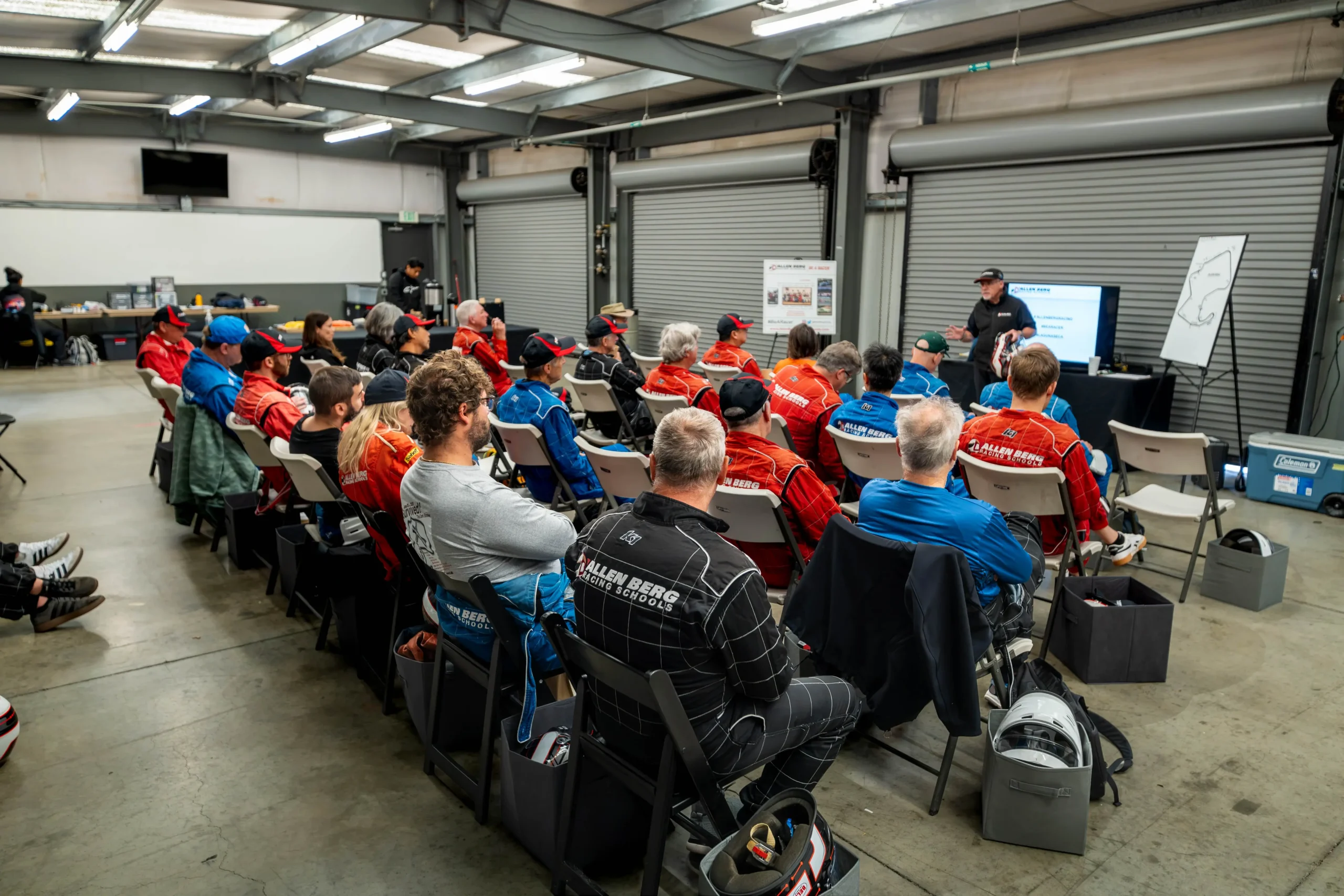 Wide shot of classroom participants suited up and watching an instructor give a presentation in the garage