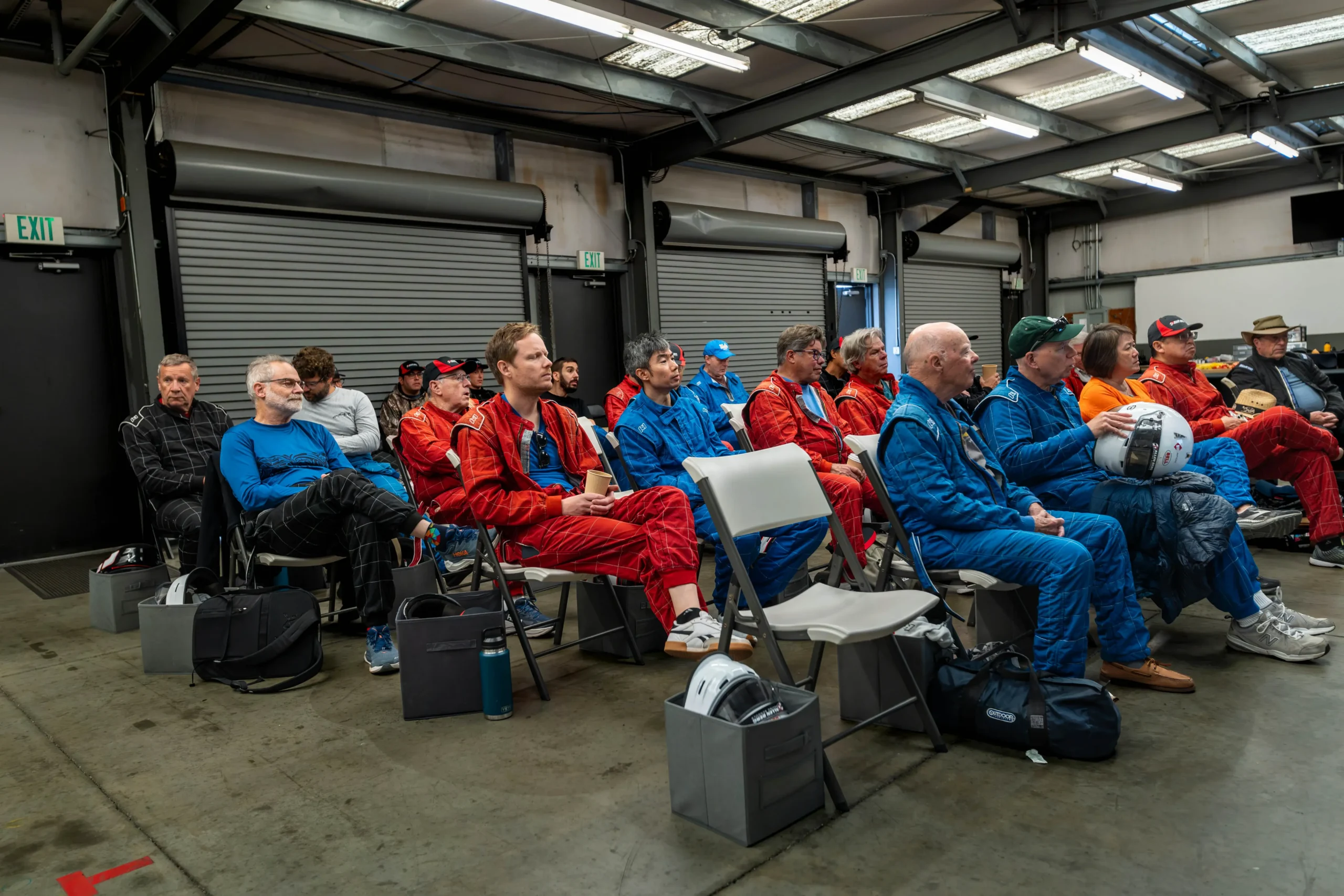 Group of race car drivers in full racing suits listening attentively during a garage classroom briefing